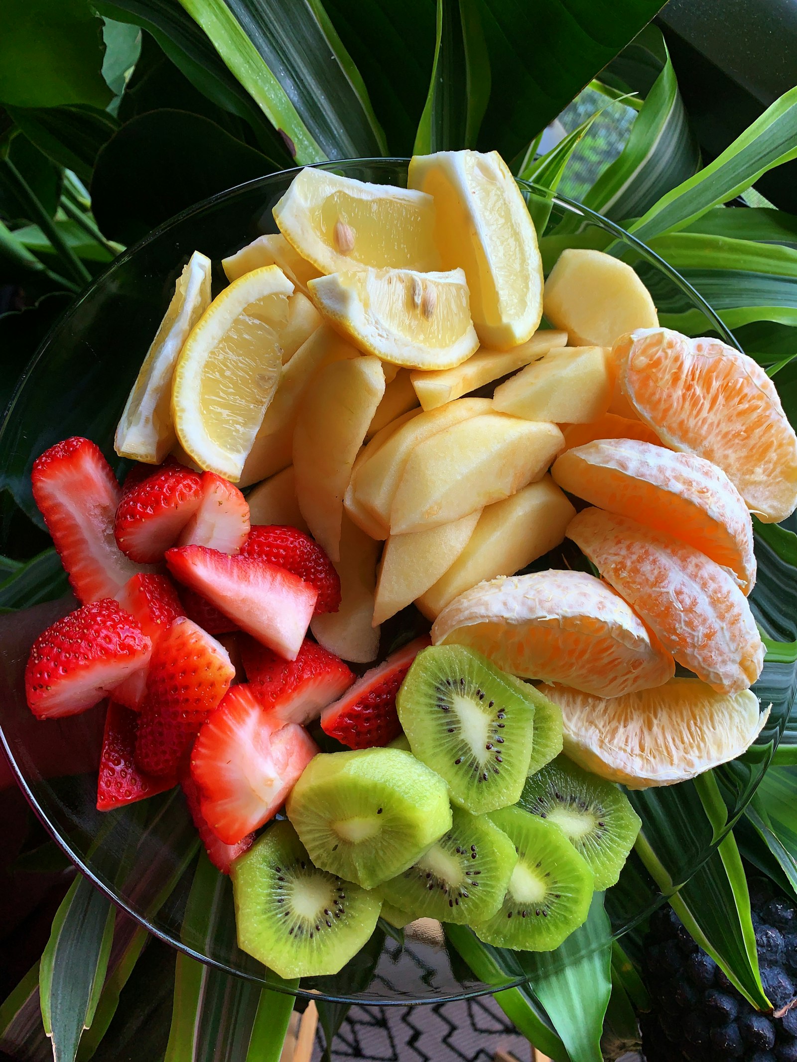 Charola de fruta fresca con fresas, kiwi, naranja, manzana y limón sobre hojas de palma